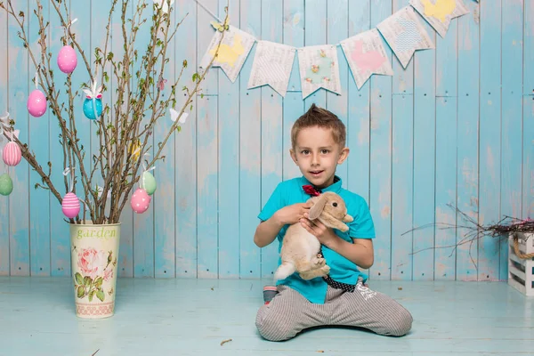 Brat chłopiec wraz z królika, siedząc na podłodze lub na krzesło w jasny niebieski odzież Wielkanoc, jaja, uroczysty nastrój, emocje i uśmiech niespodzianka wakacji letnich — Zdjęcie stockowe