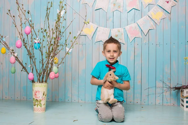 Little boy brother along with rabbit sitting on the floor or chair in bright blue clothes Easter, eggs, festive mood, emotion and smile surprise holiday celebration — Stock Photo, Image