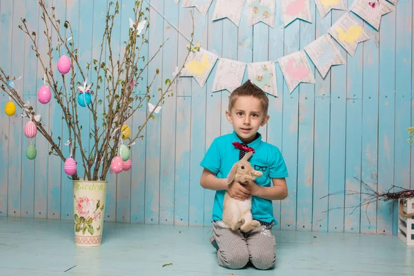 Little boy brother along with rabbit sitting on the floor or chair in bright blue clothes Easter, eggs, festive mood, emotion and smile surprise holiday celebration — Stock Photo, Image