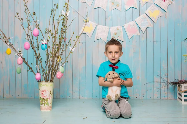 Little boy brother along with rabbit sitting on the floor or chair in bright blue clothes Easter, eggs, festive mood, emotion and smile surprise holiday celebration — Stock Photo, Image