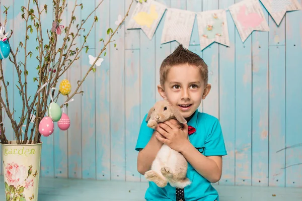 Little boy brother along with rabbit sitting on the floor or chair in bright blue clothes Easter, eggs, festive mood, emotion and smile surprise holiday celebration — Stock Photo, Image