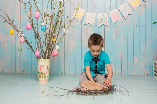 Little boy brother along with rabbit sitting on the floor or chair in bright blue clothes Easter, eggs, festive mood, emotion and smile surprise holiday celebration — Stock Photo, Image