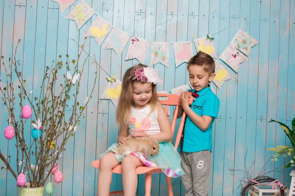 Dos niños pequeños, niño, niña, hermano y hermana junto con el conejo sentado en el suelo en ropa azul brillante Pascua, huevos, humor festivo, emoción y sonrisa fiesta sorpresa celebración —  Fotos de Stock