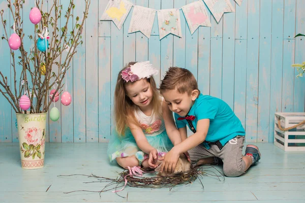 Dwa małe dzieci, chłopak, Dziewczyna, brat i siostra wraz z królika, siedząc na podłodze w jasny niebieski ubrania Wielkanoc, jaja, uroczysty nastrój, emocje i uśmiech niespodzianka wakacji letnich — Zdjęcie stockowe