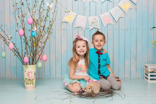 Två små childs, pojke, flicka, bror och syster tillsammans med kaninen sitter på golvet i ljusa blå kläder påsk, ägg, festlig stämning, känslor och leende överraskning semester firande — Stockfoto