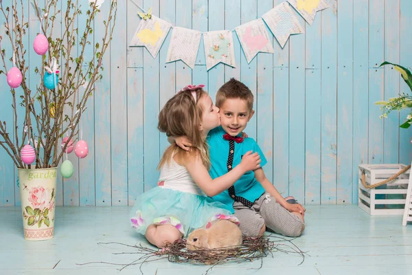 Dos niños pequeños, niño, niña, hermano y hermana junto con el conejo sentado en el suelo en ropa azul brillante Pascua, huevos, humor festivo, emoción y sonrisa fiesta sorpresa celebración —  Fotos de Stock