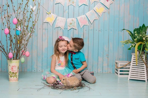 Two little childs, boy, girl, brother and sister along with rabbit sitting on the floor in bright blue clothes Easter, eggs, festive mood, emotion and smile surprise holiday celebration — Stock Photo, Image