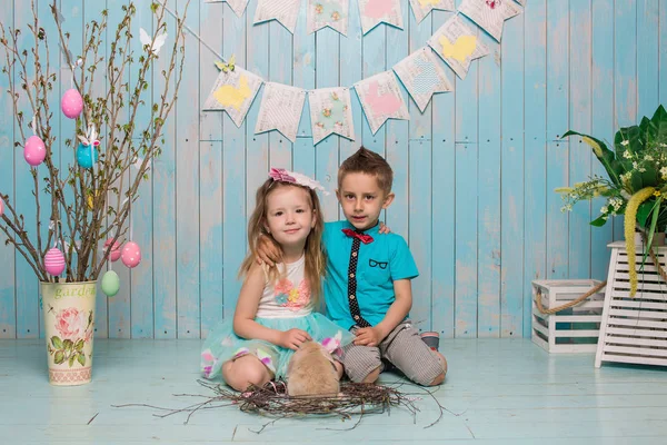 Dos niños pequeños, niño, niña, hermano y hermana junto con el conejo sentado en el suelo en ropa azul brillante Pascua, huevos, humor festivo, emoción y sonrisa fiesta sorpresa celebración —  Fotos de Stock