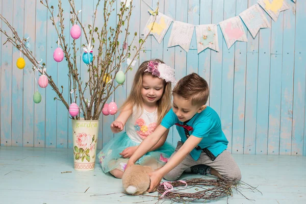 Two little childs, boy, girl, brother and sister along with rabbit sitting on the floor in bright blue clothes Easter, eggs, festive mood, emotion and smile surprise holiday celebration — Stock Photo, Image