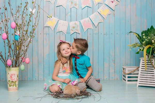 Twee kleine childs, jongen, meisje, broer en zus samen met konijn zittend op de vloer in helder blauwe kleding Pasen, eieren, feestelijke stemming, emotie en glimlach verrassing vakantie feest Stockafbeelding