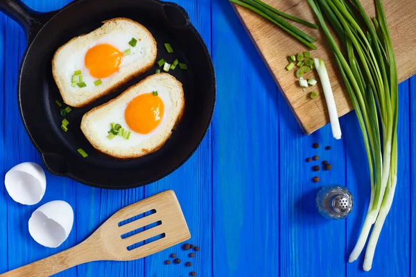 Huevos fritos en pan tostado con especias y cebolla de primavera sobre madera azul —  Fotos de Stock