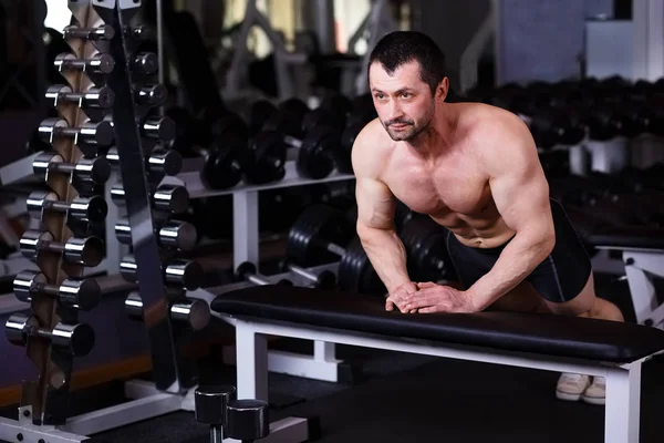 Strong healthy adult ripped man with big muscles pushing up in g