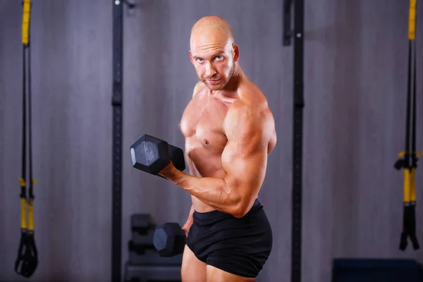 Young healthy bald ripped man with big muscles training with dum