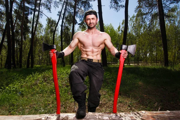 Operaio boscaiolo in piedi nella foresta con due grandi assi — Foto Stock