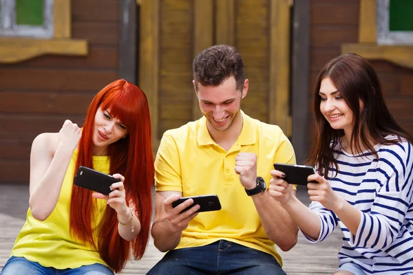 Group of three friends play mobile video game outdoors, winners
