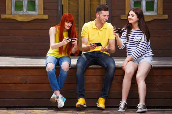 Three young happy friends playing mobile video game outdoors