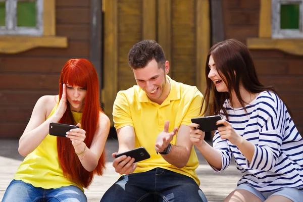 Group of three friends play mobile video game outdoors, girl and