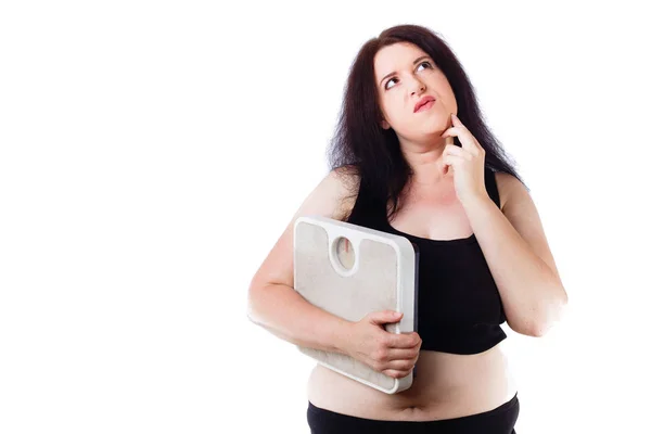 Young overweight thoughtful woman holding scale in hand — Stock Photo, Image
