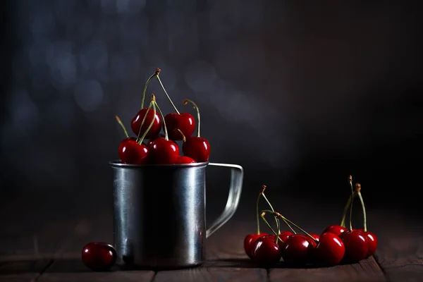Frische Kirschen in Metallbecher auf Tisch auf dunklem Hintergrund — Stockfoto