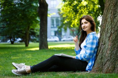 Kalemle bir parkta oturan güzel genç esmer kadın ve