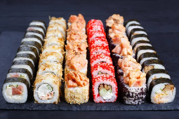 Sushi multicolorido apetitoso definido em ardósia preta, close-up. Bandeja — Fotografia de Stock