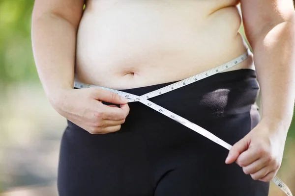 Надмірна вага жінки, що вимірює живіт за допомогою вимірювальної стрічки, близько — стокове фото