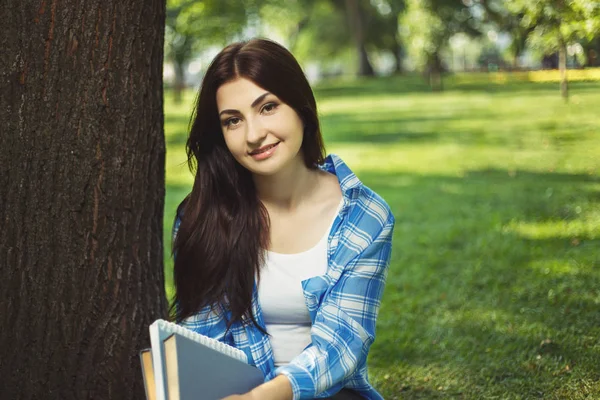 Kitaplar ile parkta oturan genç sevimli gülümseyen öğrenci kadın — Stok fotoğraf