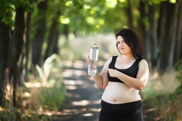 Mujer gorda con sobrepeso señalando una botella de agua en su mano . — Foto de Stock