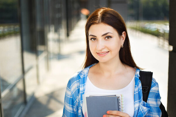 Student girl with books and backpack standing near modern facade