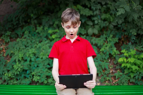 Electronic games addiction. Surprised shocked boy with tablet in hands. Education, childhood, family and people concept.