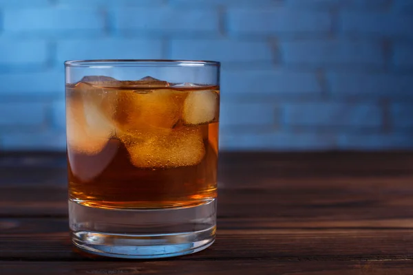 Whisky z kostkami lodu na drewnianym stole na cegły tle muru, — Zdjęcie stockowe