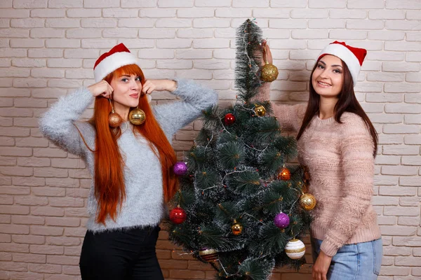 Two beautiful young women in Santa caps decorating Christmas tre — Stock Photo, Image