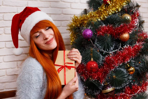 Beautiful young redhead girl in Santa cap holding a gift box sit — Stock Photo, Image