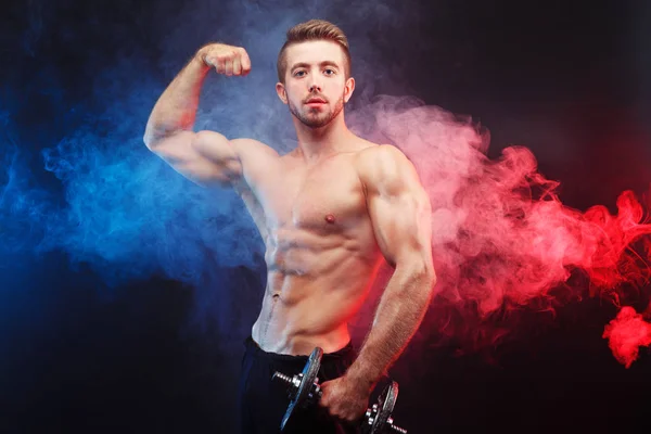 Forte atletico giovane uomo con enormi muscoli in posa con manubri — Foto Stock
