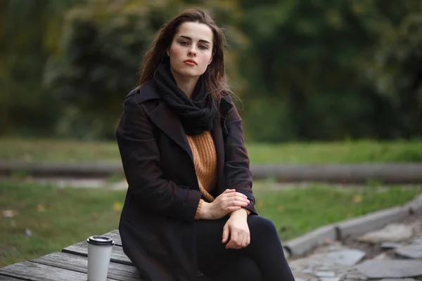 秋に座っているスタイリッシュな市松模様のコートを着ている若い女性 — ストック写真