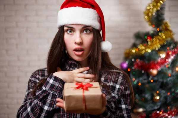 Young cute excited woman in Santa cap with a gift box in hand. N