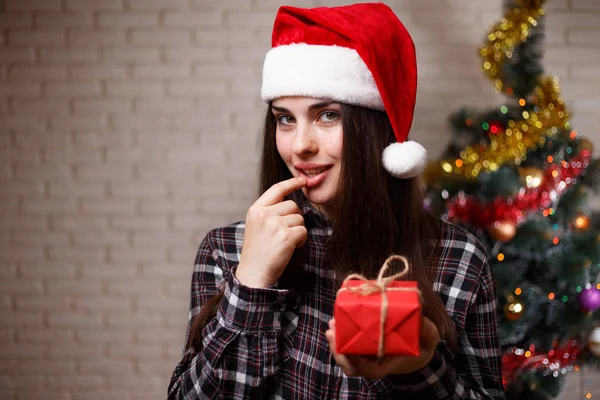 Young cute woman in Santa cap got a present on christmas tree ba — Stock Photo, Image