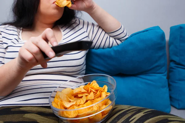 Mujer gorda con sobrepeso sentada en el sofá, comiendo papas fritas mientras wat — Foto de Stock