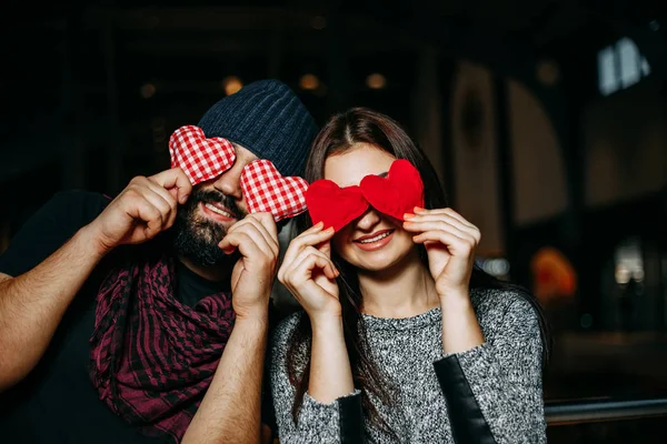 Feliz joven pareja cubriendo los ojos con corazones de almohada roja y sonrisas —  Fotos de Stock