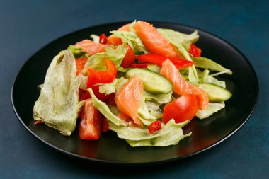 Lezzetli taze sebze salatası somon siyah plaka üzerinde iyileşmek