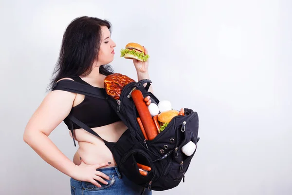 Mujer joven gorda obesa con una gran mochila llena de comida chatarra en —  Fotos de Stock