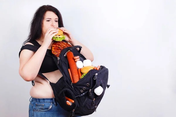 Ожирна товста молода жінка з великим рюкзаком, повним нездорової їжі на — стокове фото