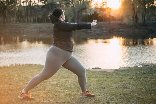 Толстая женщина расслабляется, занимаясь йогой в парке — стоковое фото