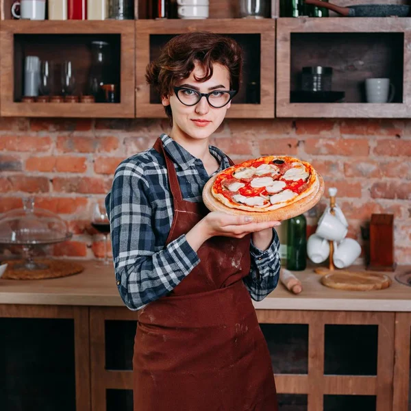 Young woman baker with freshly baked pizza