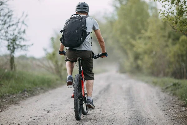 Homem de capacete montando uma bicicleta na estrada de campo — Fotografia de Stock