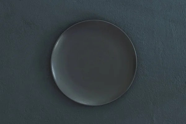 Empty black plate on dark stone background.