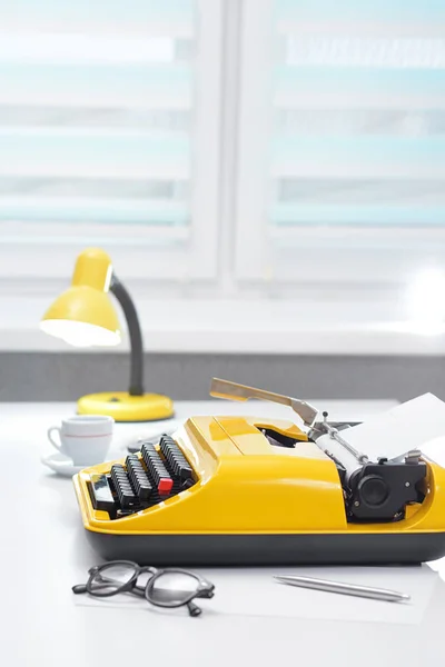 Máquina de escribir amarilla con lámpara y café en escritorio de oficina blanco —  Fotos de Stock