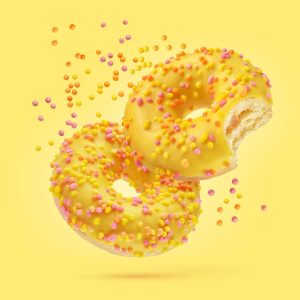 黄色の背景に飛ぶスプリンクル付きの2つの釉ドーナツ — ストック写真