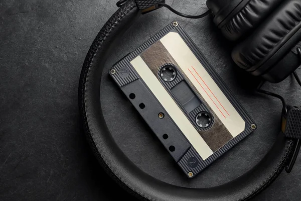 Black on-ear headphones and audio tape compact cassette on slate background