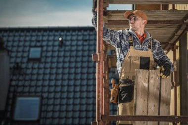 Siyah Seramik Çatı Döşemeleri ile Kaplama Evi. 30 'lu yaşlarındaki Kafkasyalı müteahhit yapı iskelesinde.. 
